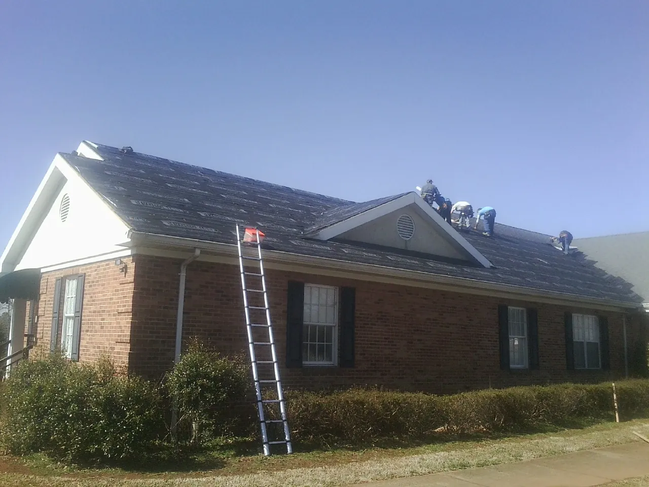 Crew tearing shingles off a brick ranch roof with a ladder set — Emergency Roof Repair work by our crew in Pittstown