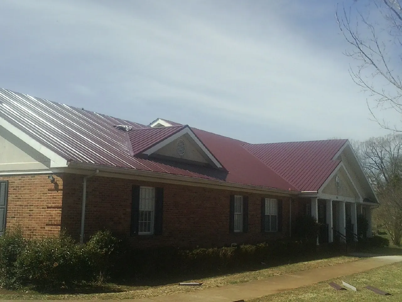 Red metal roof with gabled entries on a long brick building, from a Hail Damage Roof Repair job in Pittstown
