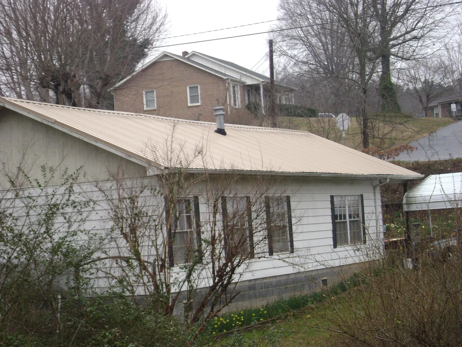 Tan metal roof on a white sided house set into a hillside — Commercial Roofing by Roofing Brothers in Pittstown